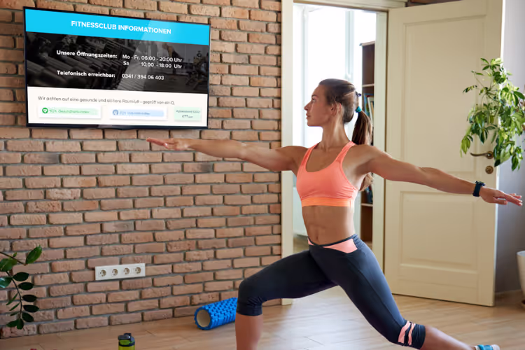 Frau in Sportbekleidung macht vor einem Bildschirm Übungen, auf dem die Parameter der Luftqualität durch die air-Q Smart Widgets angezeigt werden