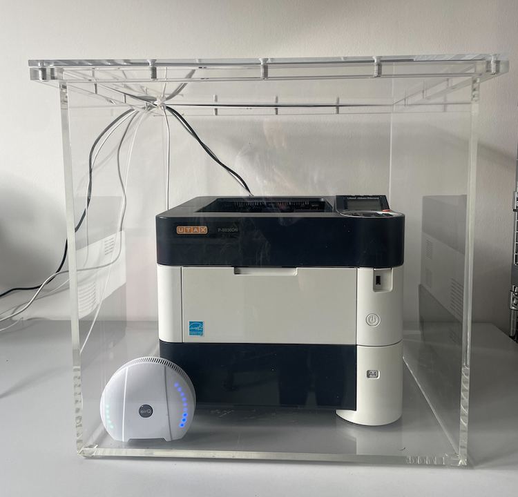 Laserdrucker und Luftmessgerät air-Q in einer durchsichtigen Box