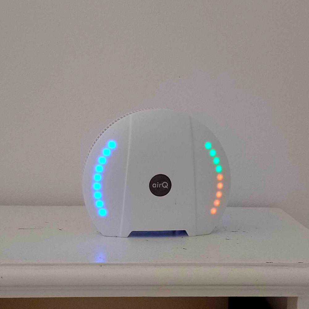 Luftmessgerät air-Q mit leuchtenden LED-Anzeigen auf einem weißen Regal